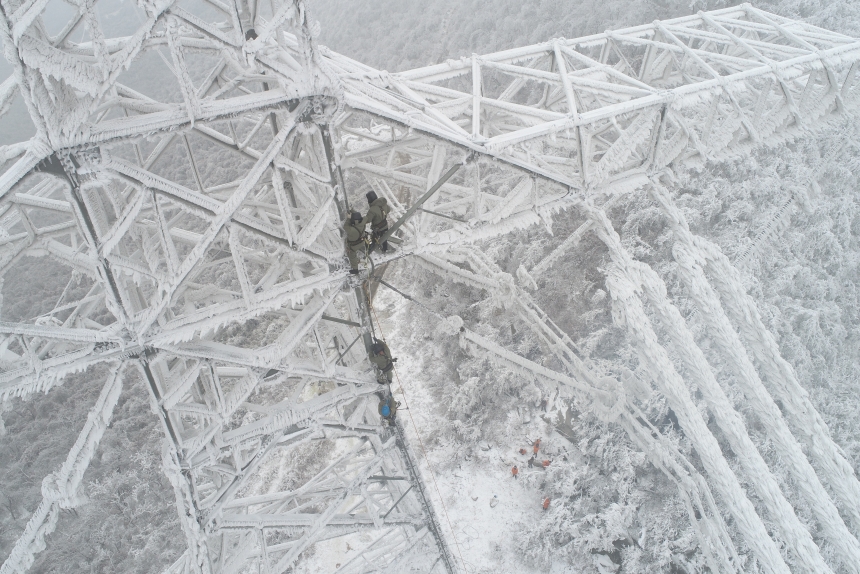 電力應(yīng)急處置人員爬上70米高的±800千伏陜武輸電線路1898號塔，通過機械震動方式清除地線和光纜上的積雪。鄒小民攝 